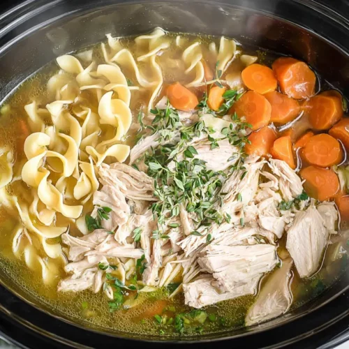 A steaming bowl of Crockpot Chicken Noodle Soup garnished with fresh parsley.