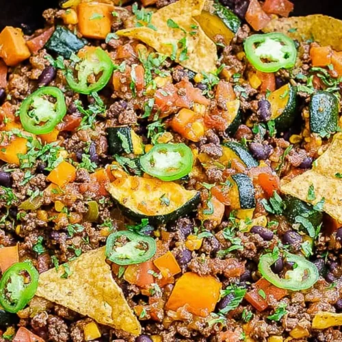 A close-up of a sizzling ground beef veggie skillet with vibrant vegetables.