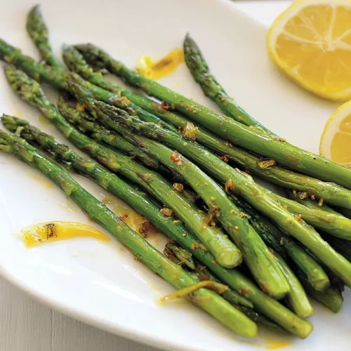 A pile of vibrant green lemony asparagus stalks on a white plate.