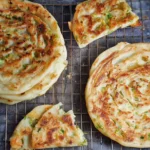 Several thin and flaky crispy Cong You Bing stacked on a plate.