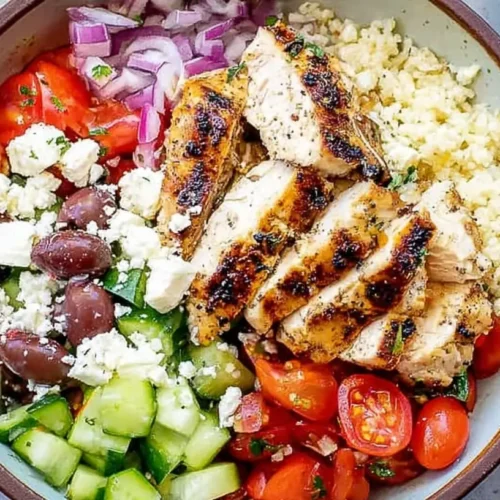A vibrant Greek chicken bowl with fresh vegetables and feta cheese