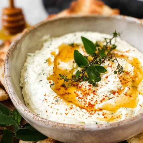 A creamy ricotta dip drizzled generously with hot honey, served in a ceramic bowl.