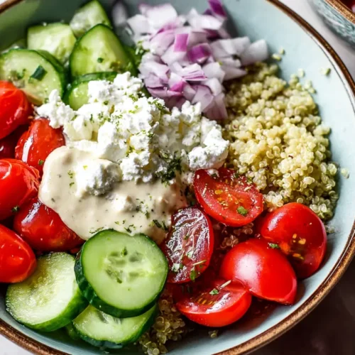 A Mediterranean quinoa bowl featuring fresh cucumbers, ripe tomatoes, and a hummus drizzle.