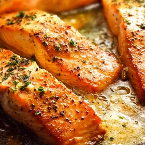 A perfectly cooked garlic butter salmon skillet with herbs and lemon slices.