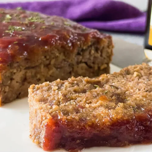 A baked old-fashioned meatloaf recipe, sliced and ready to serve on a white plate.