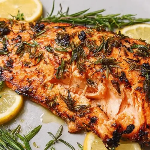 Simple salmon fillet seasoned with lemon slices and fresh herbs on a cooking sheet.